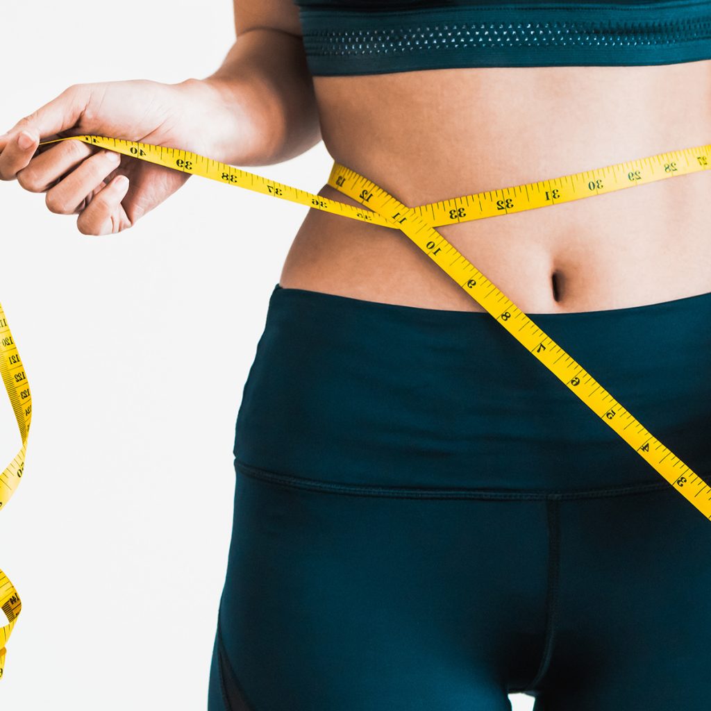 Cropped view of slim woman measuring waist with tape measure at home, close up. Unrecognizable european woman checking the result of diet for weight loss or liposuction indoors | Avail Aesthetics in Cary, Raleigh & Wake Forest, NC